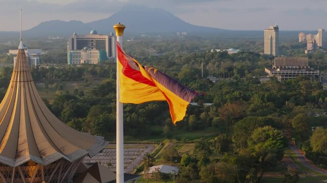 Iconic view of the Sarawak state flag flying next to the golden dome of the Sarawak State Legislative Assembly during evening golden hour.