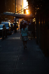Silhouette of a woman walking away at sunset on a city street.