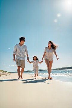 Young asian family walking along a beach enjoying a family day out on a vibrant blue sky day