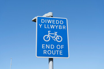 Blue sign with a bicycle symbol and the words 'end of route' in English and Welsh against a clear blue sky.