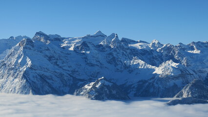 Fototapeta premium Stunning panoramic view of snow-capped peaks and clouds. Perfect for winter, nature, and travel themes.