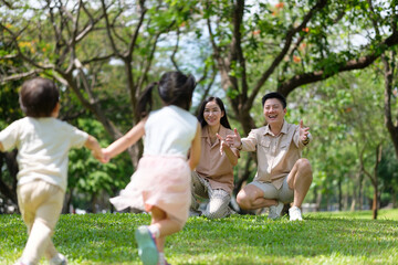 Fototapeta premium Two children joyfully run toward their parents with arms wide open in a sunny green park.