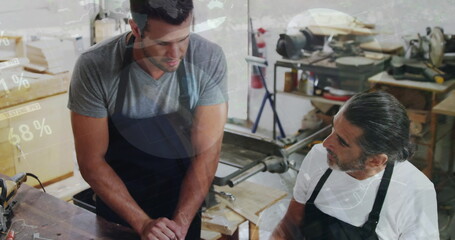 Image of financial graphs over caucasian men working in carpentry workshop