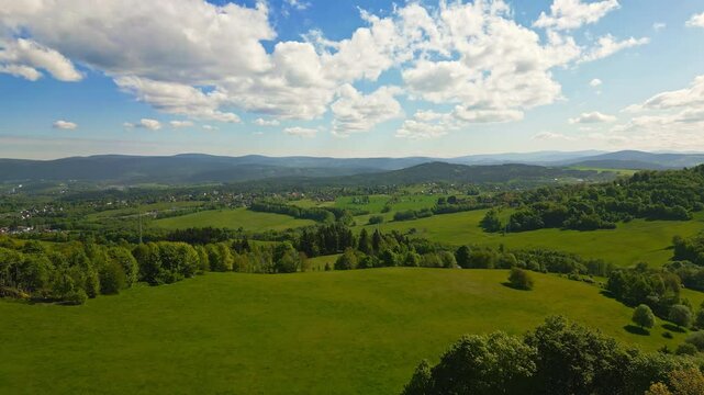 Aerial summer flight over lush green meadows and forests near Jested mountain with distant view of Jizera Mountains and picturesque villages scattered across the landscape
