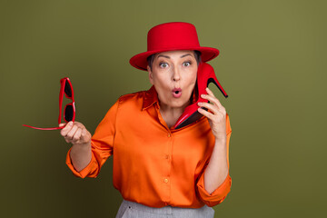 Confident woman in vibrant fashion holding red accessories against khaki background, expressing...