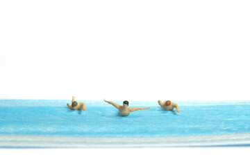 Miniature people toy figure photography. Creative concept. A group of young men swimmer doing freestyle swimming competition above blue face mask, isolated white background