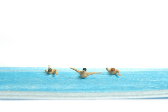 Miniature people toy figure photography. Creative concept. A group of young men swimmer doing freestyle swimming competition above blue face mask, isolated white background