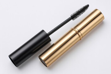 Black mascara brush and golden tube lying on white background