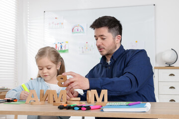 Little girl learning letters with teacher at desk indoors