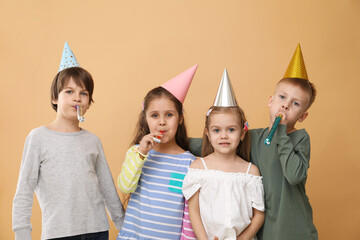 Children in conical paper hats with blowers on beige background. Birthday surprise party