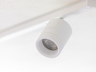 White cylindrical spotlight hanging from ceiling track lighting system