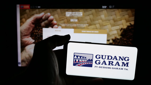 Stuttgart, Germany - 05-02-2025: Person holding mobile phone with logo of Indonesian tobacco company Gudang Garam on screen in front of web page. Focus on phone display.