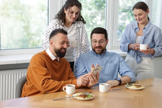 Man showing his colleagues something on smartphone during lunch break in office - Powered by Adobe