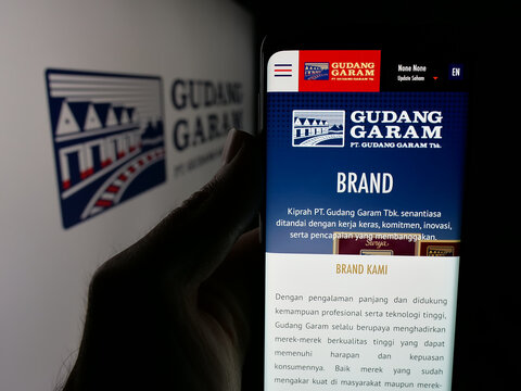 Stuttgart, Germany - 05-02-2025: Person holding cellphone with web page of Indonesian tobacco company Gudang Garam on screen in front of logo. Focus on center of phone display.