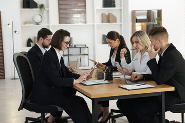 Coworkers with different devices working together at wooden table in office