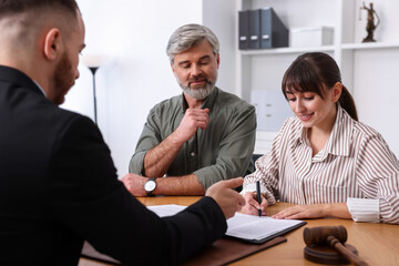 Clients signing notarial paperwork during meeting with lawyer at wooden desk indoors