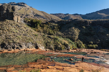 Man standing by the rocky, shallow Agrio River with mountains rising. Neuquen, Argentina