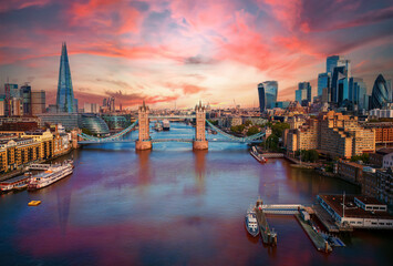 Aerial view of Tower Bridge and modern London skyline at sunset, showcasing iconic landmarks, vibrant colors, and the bustling Thames River