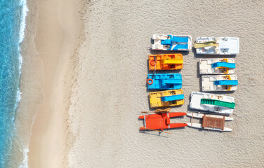 Aerial view of colorful catamarans on empty sandy beach and blue sea with waves on summer sunny...