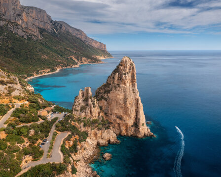 Fototapeta Aerial view of rock and mountains, blue sea bay, beach, boat on sunny summer day. Sardinia Island, Italy. Top drone view of cliffs, stones, green trees, road, transparent water at sunset. Landscape