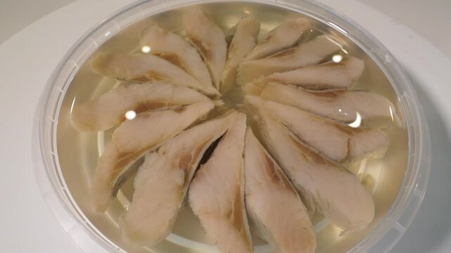 Fish in oil in plastic container, close-up. Herring fish macro shot. Slow motion.