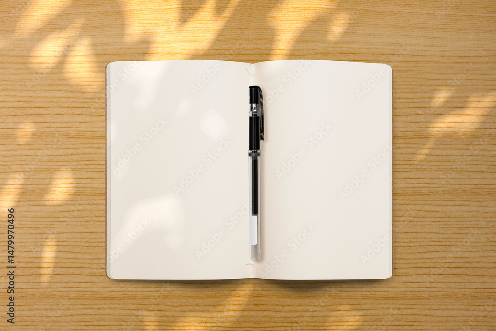 Poster top view of an open notebook and a pen with shadow on a wooden background. blank paper or sheet. moc