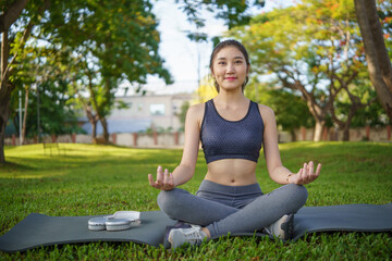 Calm young woman in activewear practicing yoga on a mat in a peaceful green park.