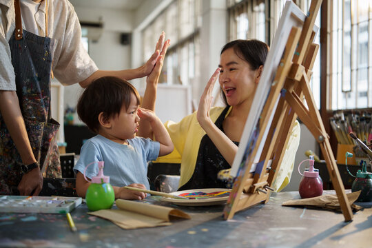 Boy painting on canvas with support from mother and teacher in an art classroom.