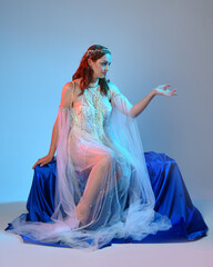 Fantasy studio portrait of a red-haired mermaid faery model wearing a white pearl gown, fairytale...
