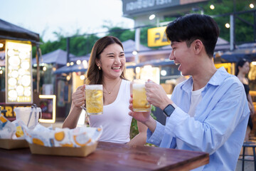 Happy couple toasting with beer at a vibrant street food market.
