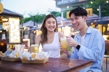 Joyful couple toasting with beer while enjoying street food at an outdoor market.