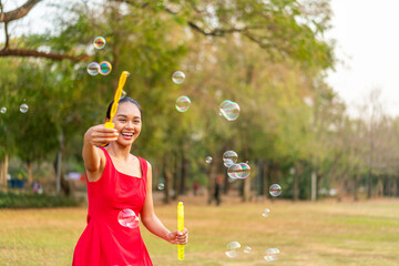 Happy Asian Woman in Red Dress Playing with Bubbles in Sunny Park