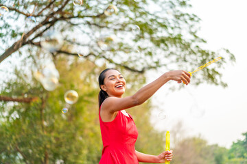 Happy Asian Woman in Red Dress Playing with Bubbles in Sunny Park