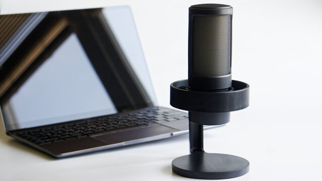 Studio condenser microphone positioned next to an open laptop on a white surface, ideal for podcast creation, live streaming and voiceover recording projects. Photo, selective focus