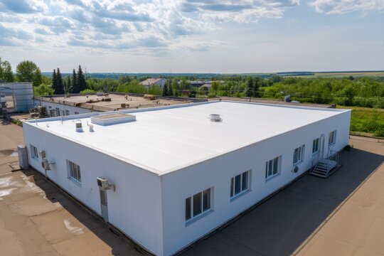 Aerial view of white commercial building with flat roof and air conditioning units in rural setting under cloudy sky