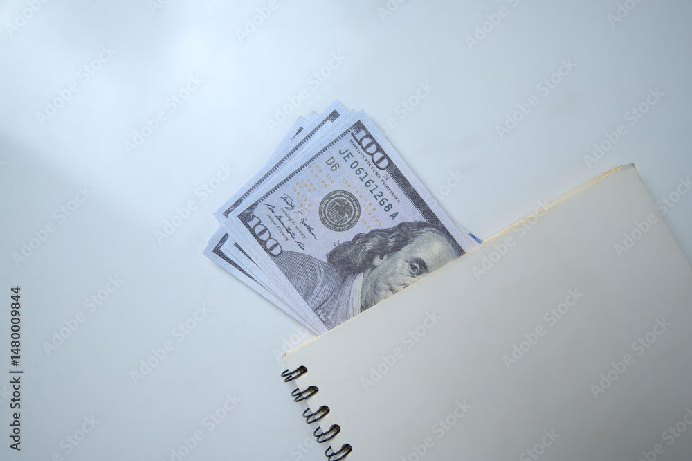 Poster top view of a pile of 100 dollar banknotes on a notebook with a white background. copy space. concep