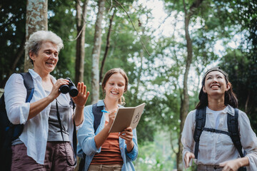 Group of diverse women exploring nature, smiling and studying wildlife in the forest, holding...
