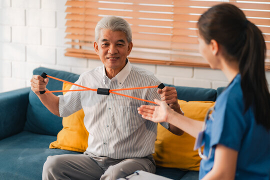 Senior man exercises with resistance band under guidance of a healthcare professional, promoting physical therapy, wellness, and preventive health care in a supportive home environment
