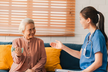 Smiling senior woman exercising with dumbbell under guidance of young nurse during rehabilitation therapy session at home, elderly care health insurance physical recovery wellness support