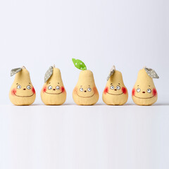 Five smiling pear-shaped fabric toys with cartoon faces stand in a row on white background