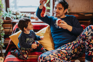 Obraz premium A father and his young child enjoying quality time together while unwrapping presents in a cozy and festive holiday atmosphere, highlighting family warmth and celebration.