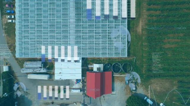 Large glass greenhouse showing top-down featuring red-roofed buildings, tanks, pipelines, crop rows