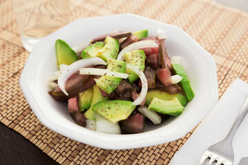 Salad of black tomatoes, avocado and onions in white ceramic bowl