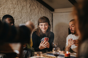 A group of friends sitting around a table playing cards, enjoying drinks and each other's company in a warm, intimate setting, perfect for relaxation and bonding time.