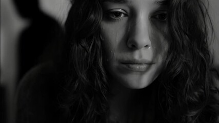 Distressed woman with tears, somber portrait in black and white, with blurred figure in background suggesting sadness and conflict