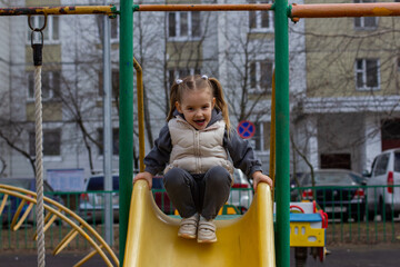 A cheerful little girl with pigtails, enjoying playing time on a hill on a city gaming platform,...