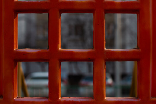 The red grid in the foreground filters the blurry urban background and creates an abstract geometric pattern filled with squares and rectangles.