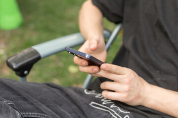 An individual is comfortably engaged with their smartphone in a peaceful outdoor setting, adopting a relaxed and casual posture