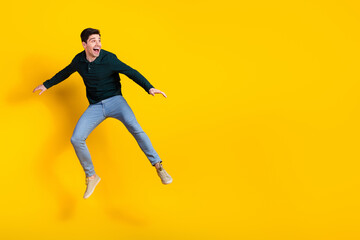 Fototapeta premium Young man jumping with joy on a yellow background wearing a green shirt and jeans showcasing happiness and vibrant energy