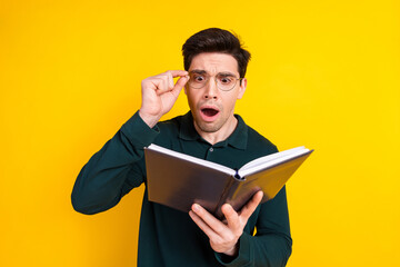 Surprised Young Man Reading a Book Standing Against a Vibrant Yellow Background, Wearing Green Casual Polo Shirt and Glasses